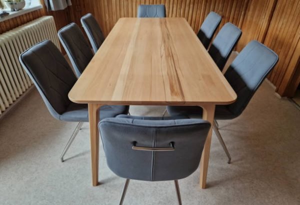 home dining table made of beech wood. around there are 8 chairs with upholstery and geometric stitching. an empty table top without a tablecloth suitable for advertising purposes.